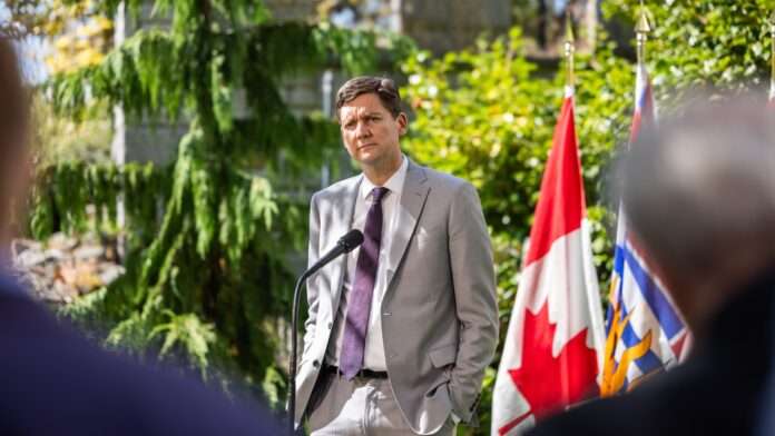 Photo of B.C. Premier David Eby standing in front of Canada and B.C. flags.